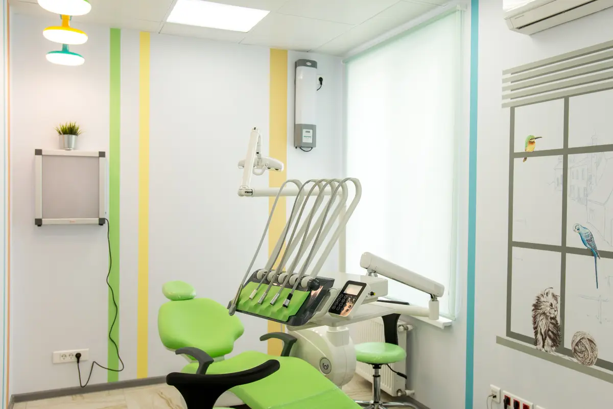 A bright dental office interior with a green treatment chair and equipment
