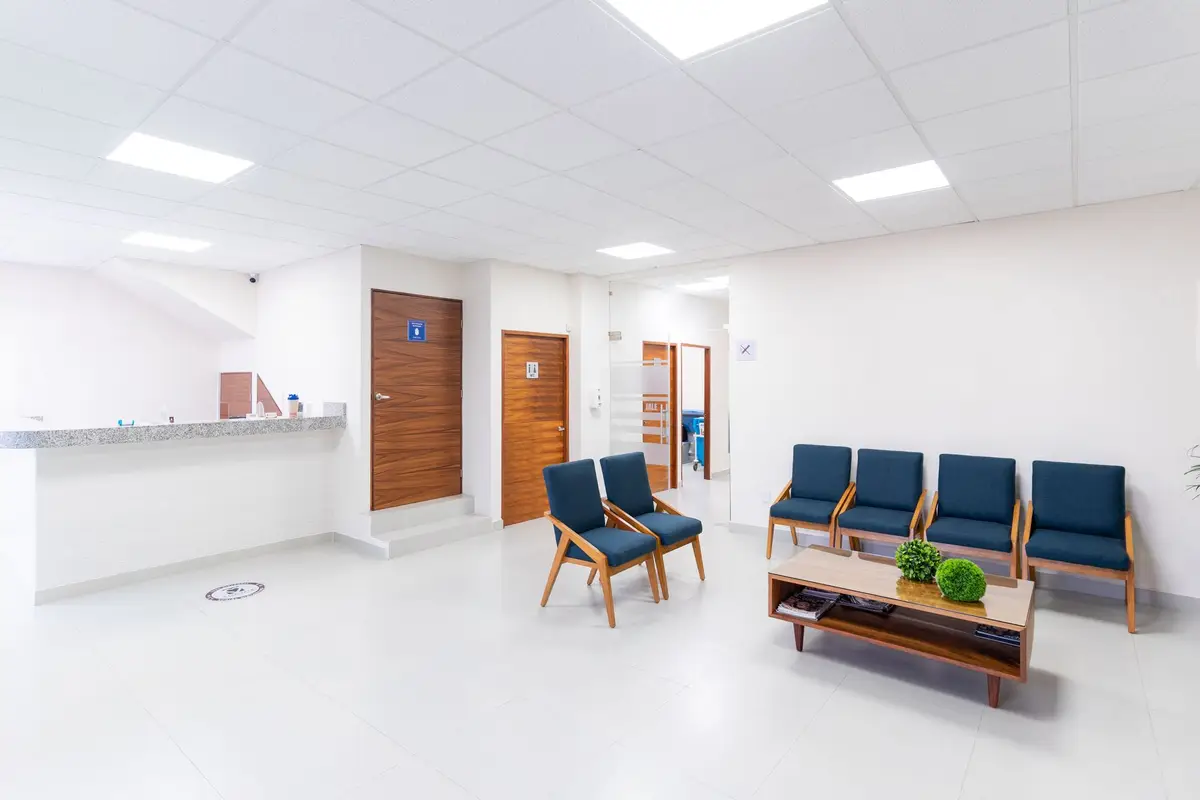 A bright, quiet practice waiting room with a row of blue chairs and a reception counter